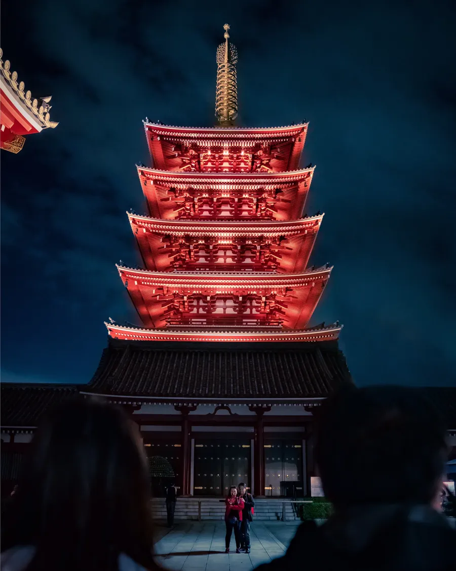 A red temple pagoda lit against a night sky.