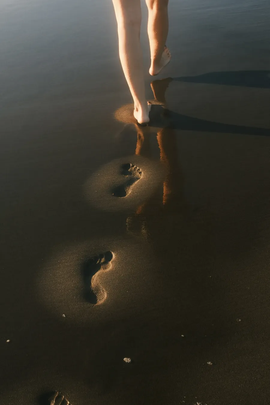 Bare feet and a line of footprints in shallow water.