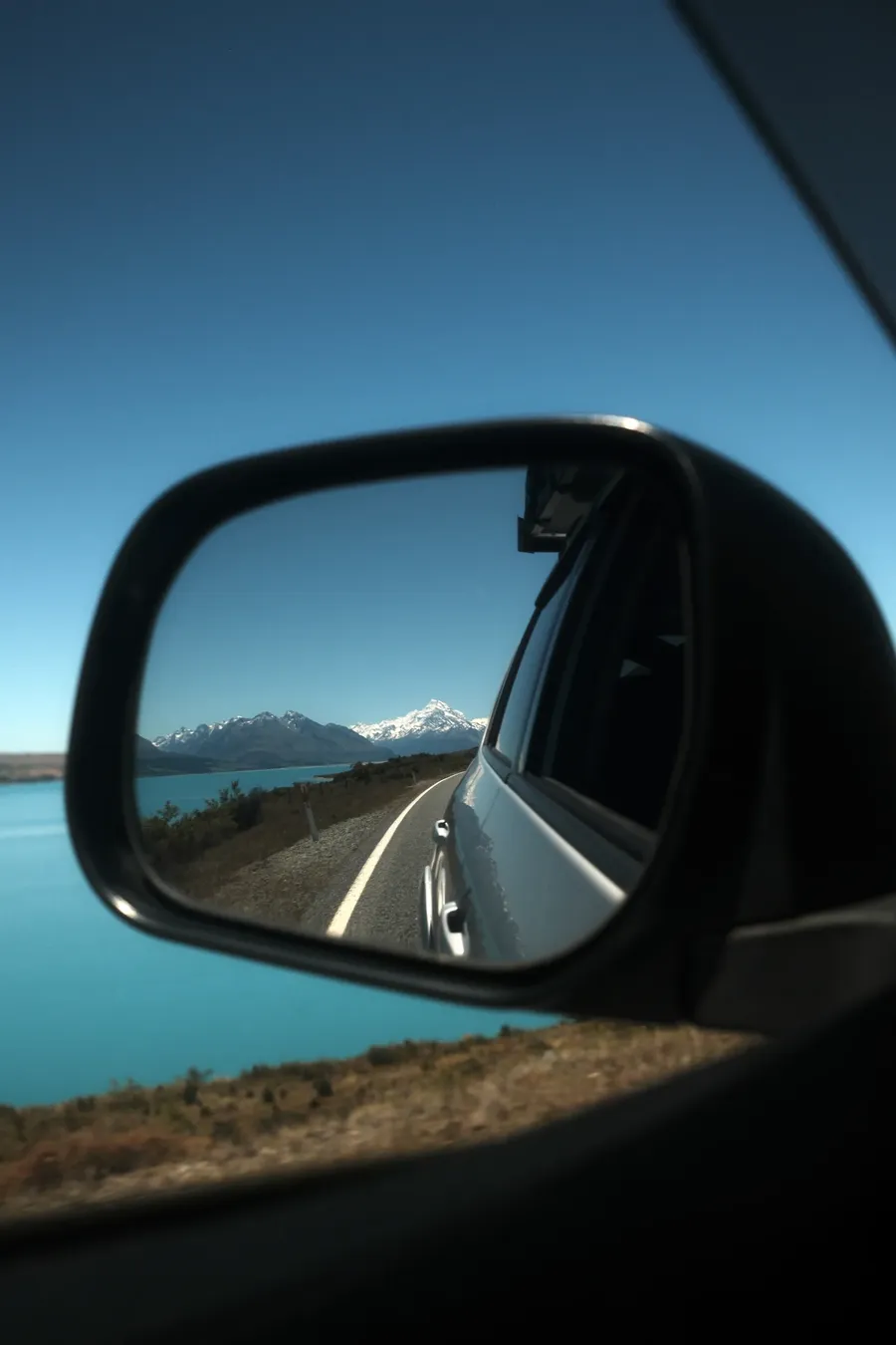 A road and a lake seen in a car wing mirror.