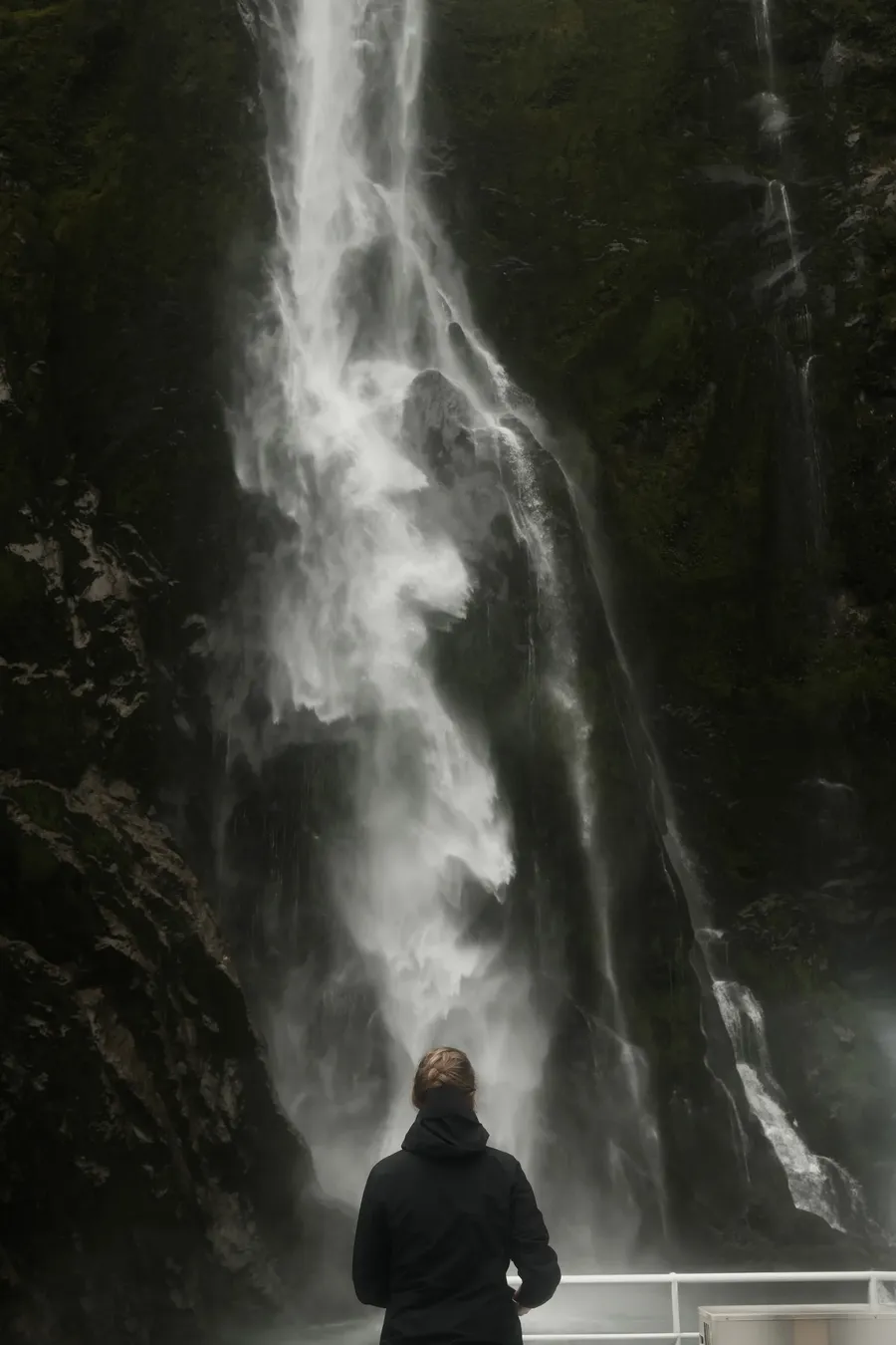 A figure standing before a waterfall.
