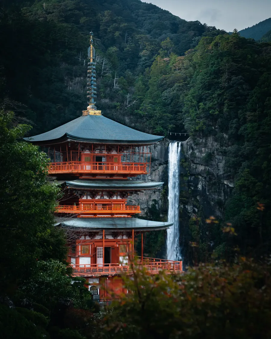 A pagoda beside a tall waterfall.