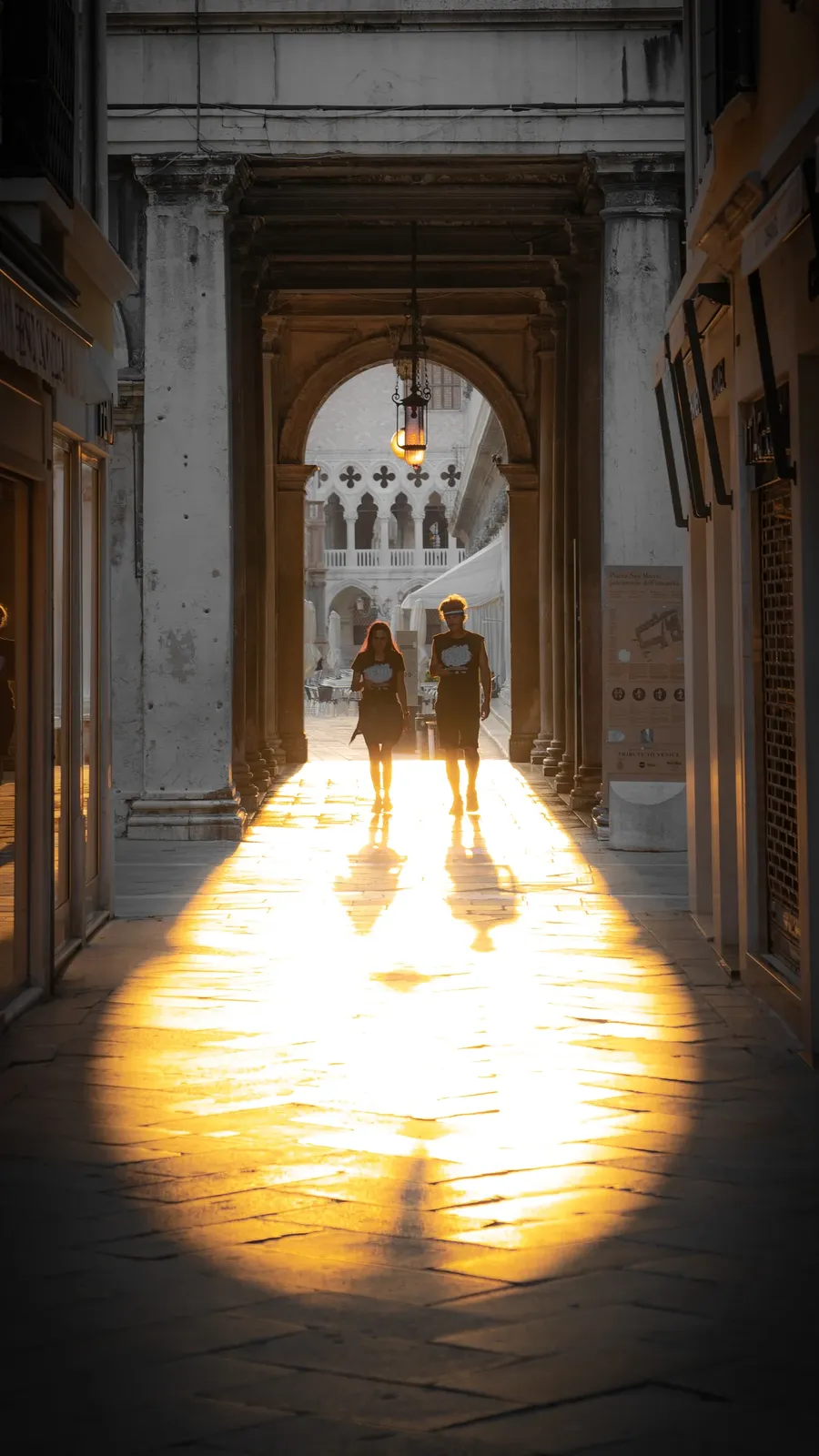 Two figures at the lit end of an arcade.